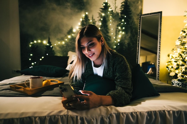 Jonge lachende blanke vrouw met behulp van mobiele telefoon in vakanties thuis op het bed.