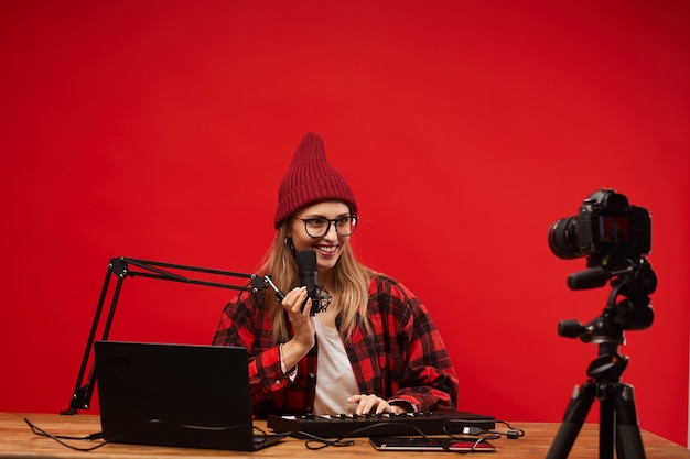 Jonge lachende blogger aan tafel zitten met laptop en muzikaal toetsenbord en zingen op de camera