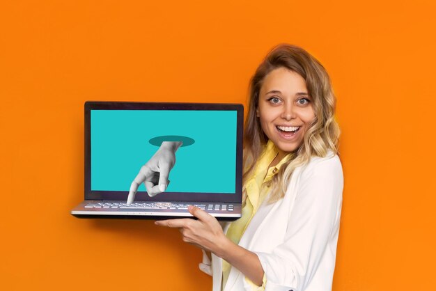 Foto jonge lachende blonde vrouw die laptop met turquoise scherm toont met standbeeldhand die op de toets drukt