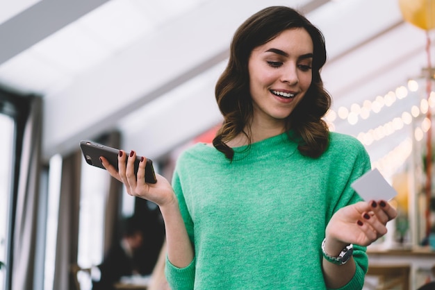 Jonge lachende brunette met visitekaartje en smartphone