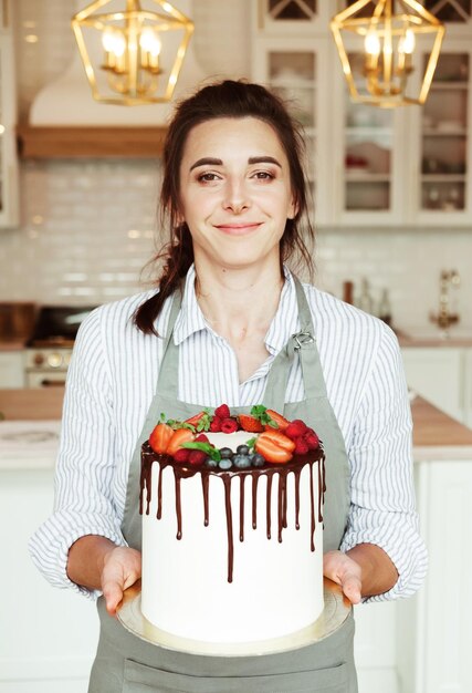 Jonge lachende brunette vrouw chef-kok met een zelfgemaakte cake versierd met chocolade en verse bessen