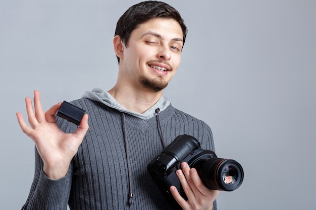 Jonge lachende fotograaf in shirt houdt de batterij vast voor DSLR