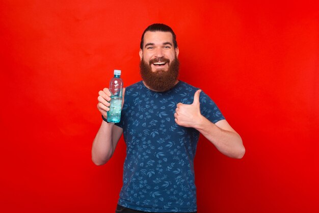 Jonge lachende man houdt en toont een fles water en duim omhoog.