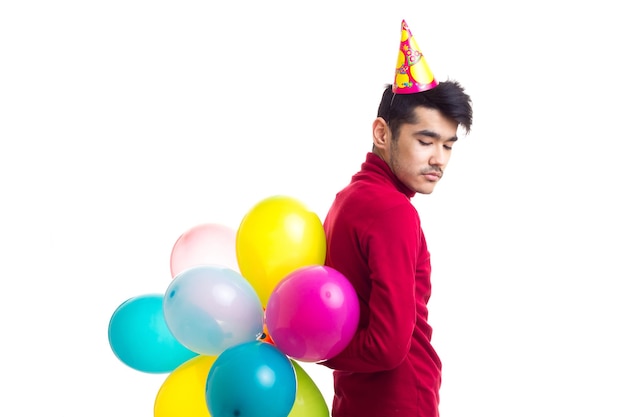 Jonge lachende man met donker haar in rood shirt met feesthoed met veel gekleurde ballonnen