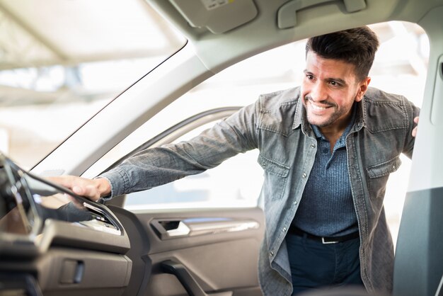 Jonge lachende man nemen van het nemen van kijken naar de auto in de showroom