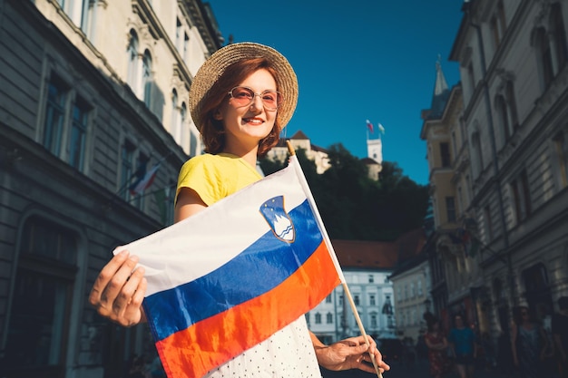 Jonge lachende meisje in zonnebril met Sloveense vlag op het centrale plein van Ljubljana Vrouw toerist met Sloveense vlag op de achtergrond van stadsarchitectuur Reizen levende studie in Slovenië Europa