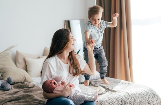 Jonge lachende moeder met pasgeboren baby en peuter zoon in bed thuis