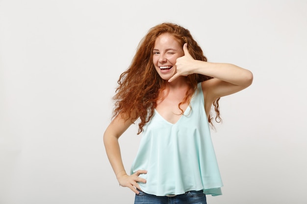 Jonge lachende roodharige vrouw in casual lichte kleding poseren geïsoleerd op een witte achtergrond in de studio. mensen levensstijl concept. bespotten kopie ruimte. telefoongebaar doen zoals zegt bel me terug, knipperend.