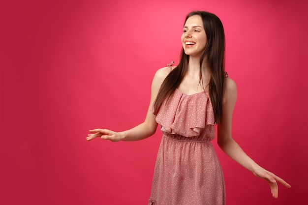 Jonge lachende vrouw dansen met uitgestrekte armen tegen roze achtergrond