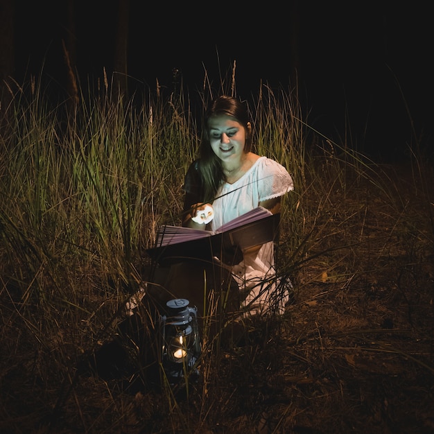 Foto jonge lachende vrouw die een magisch boek leest 's nachts bos