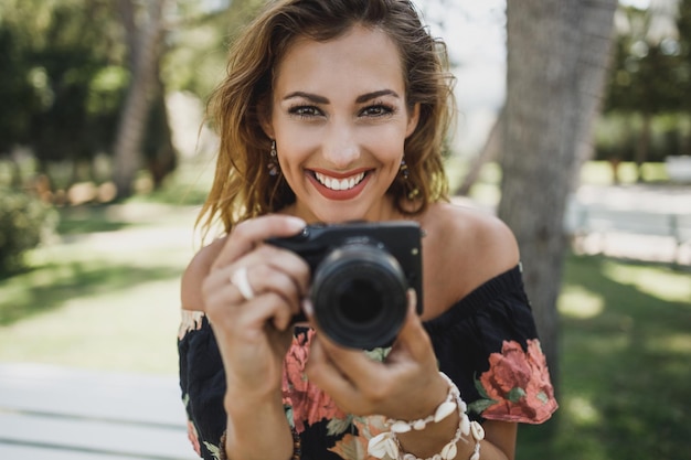 Jonge lachende vrouw die foto's maakt met haar digitale camera en naar de camera kijkt.