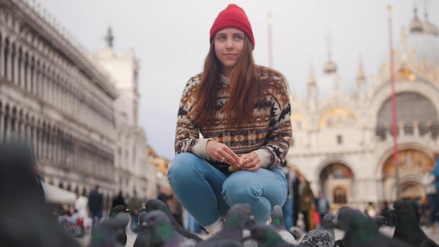 Jonge lachende vrouw hurkt in het midden van het plein bij de hangry-duiven