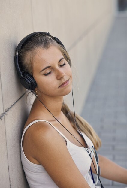 Jonge lachende vrouw in een wit T-shirt met muziek luisteren en zittend op de stoep