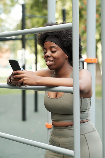 Jonge lachende vrouw in sportkleding scrollen in smartphone