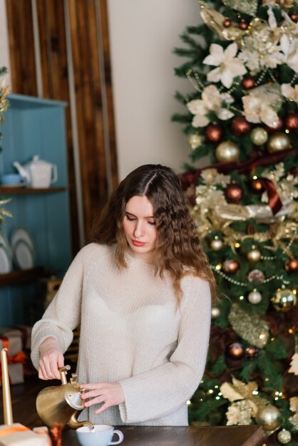 Jonge lachende vrouw in trui, wintervakantie in ingericht interieur met kerstboom.