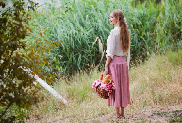 Jonge lachende vrouw in vintage retro-stijl kleding houdt een picknickmand in haar hand
