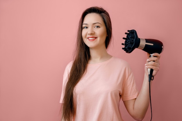 Jonge lachende vrouw met een haardroger in handen op roze achtergrond