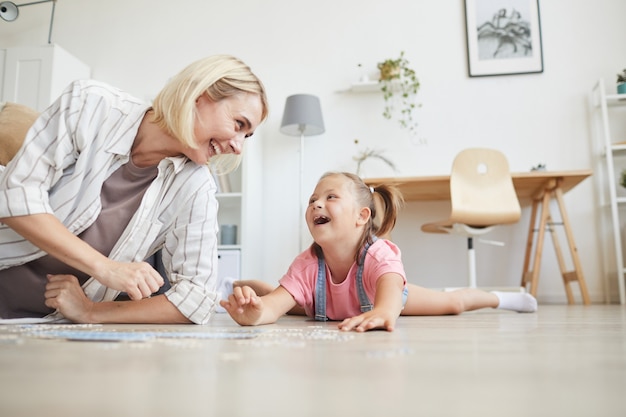 Jonge lachende vrouw tijd doorbrengen met haar dochter ze lachen terwijl liggend op de vloer en het verzamelen van puzzels thuis