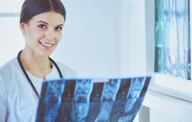 Foto jonge lachende vrouwelijke arts met stethoscoop kijken naar röntgenfoto's op spreekkamer