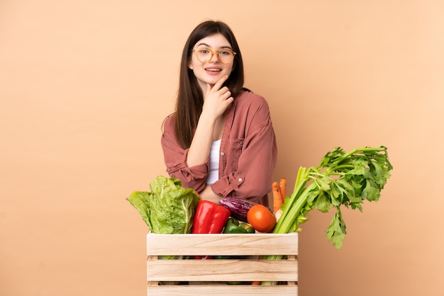 Jonge landbouwersvrouw met vers geplukte groenten in een doos met glazen en het glimlachen