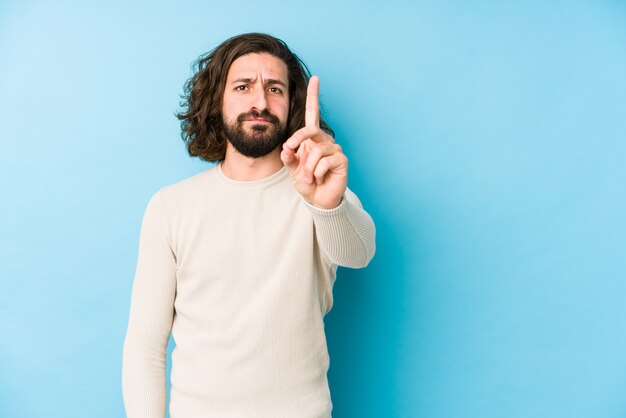 Jonge lange haarmens op een blauwe muur die nummer één met vinger toont.