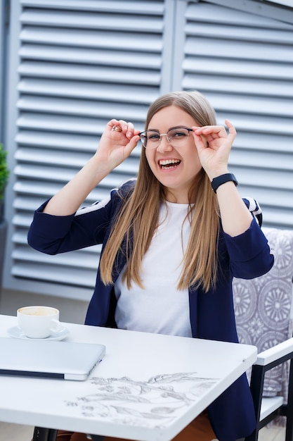 Jonge langharige vrouw die werkt met een laptop, zittend op een terras in een café. Bedrijfsontwikkelingsconcept, meisje in de lunchpauze aan het werk met een kopje koffie