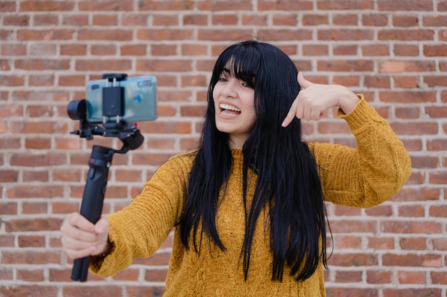 Jonge Latijns-Amerikaanse vrouw die lacht en zichzelf filmt met haar mobiele telefoon met behulp van een cardanische ophanging