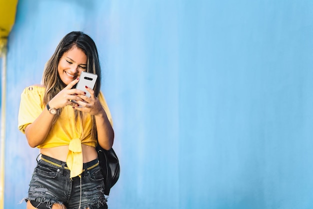 Jonge latijns-amerikaanse vrouw loopt terwijl ze een bericht schrijft met haar telefoon