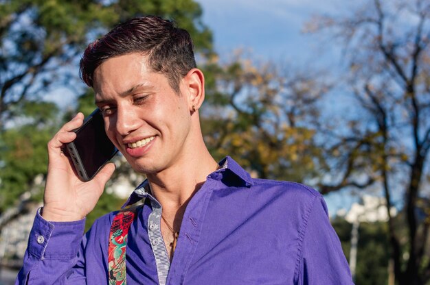 Jonge Latijns-man buiten op een zonnige dag glimlachend en pratend over het telefoontechnologieconcept