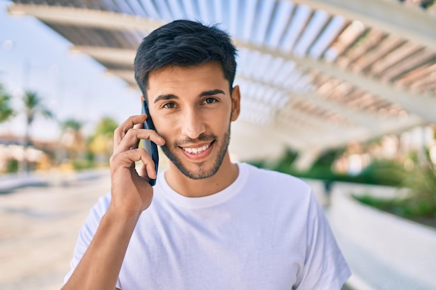 Jonge latijns-man die lacht gelukkig praten op de smartphone wandelen in de stad.