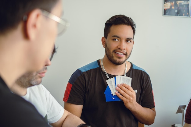 Jonge latijns-man die lacht terwijl hij zijn rivaliserende vriend in een kaartspel analyseert