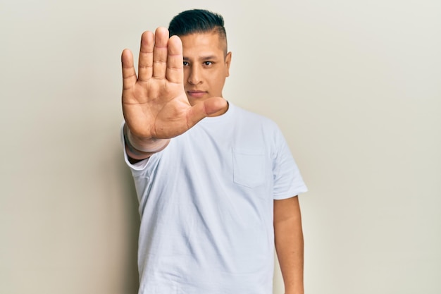 Jonge latijns-man met casual wit t-shirt doen stop zingen met handpalm waarschuwende uitdrukking met negatief en serieus gebaar op het gezicht