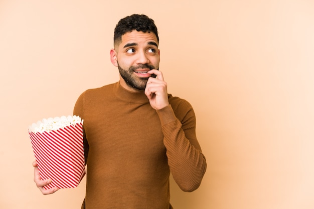 Jonge Latijns-man met een pop corn geïsoleerd ontspannen denken aan iets kijken naar een kopie ruimte.