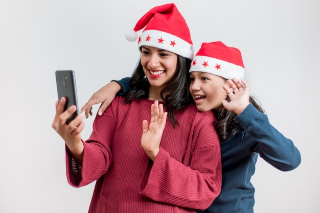 Jonge Latijns-moeder en dochter dragen kerstmutsen en voeren online een videogesprek met familie met Kerstmis. Kerstmis vieren met sociale afstand.