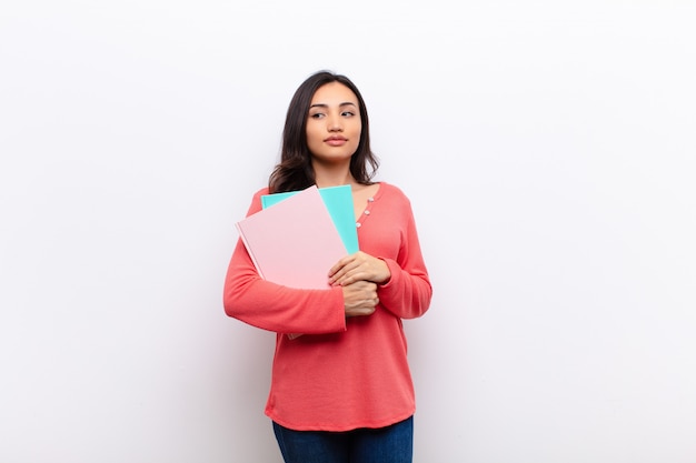 Jonge Latijns-mooie vrouw tegen vlakke muur met boeken