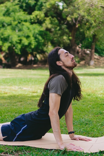 Foto jonge latijns-spaanse man die yoga beoefent en de maangroet doet met gesloten ogen en hoofd omhoog op een mat in een groen veld verticale foto