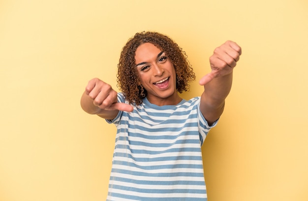 Jonge Latijns-transseksuele vrouw geïsoleerd op gele achtergrond die beide duimen opheft, glimlachend en zelfverzekerd.