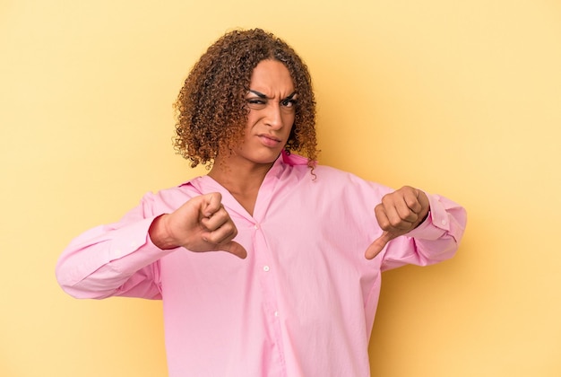 Foto jonge latijns-transseksuele vrouw geïsoleerd op gele achtergrond met duim omlaag, teleurstelling concept.