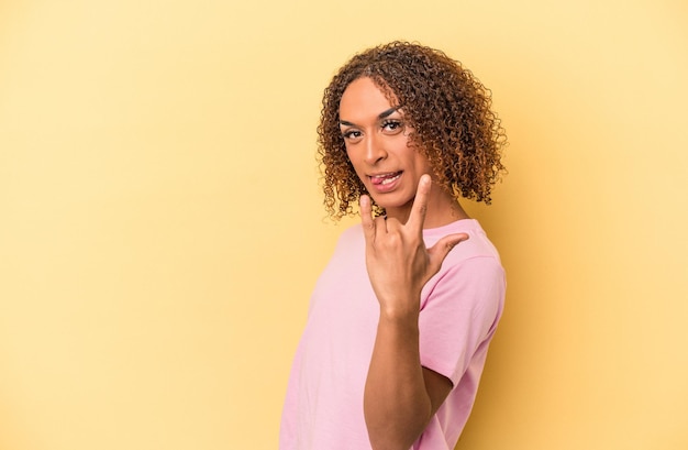 Jonge Latijns-transseksuele vrouw geïsoleerd op gele achtergrond met rock gebaar met vingers