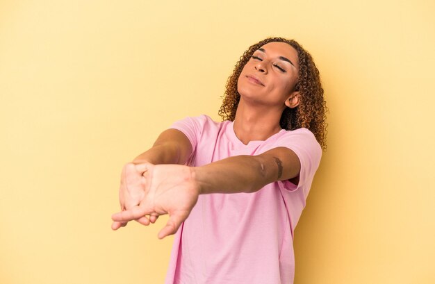 Jonge Latijns-transseksuele vrouw geïsoleerd op gele achtergrond strekkende armen, ontspannen positie.