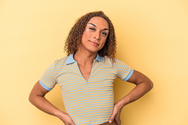 Jonge Latijns-transseksuele vrouw geïsoleerd op gele achtergrond vertrouwen houden handen op de heupen.