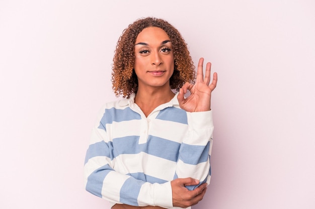 Jonge Latijns-transseksuele vrouw geïsoleerd op roze achtergrond knipoogt en houdt een goed gebaar met de hand.