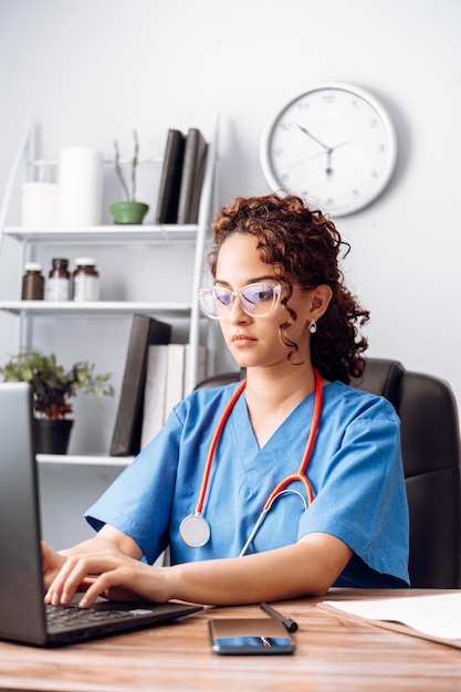 Jonge Latijns-vrouw arts in wit medisch uniform met stethoscoop met behulp van een computer laptop