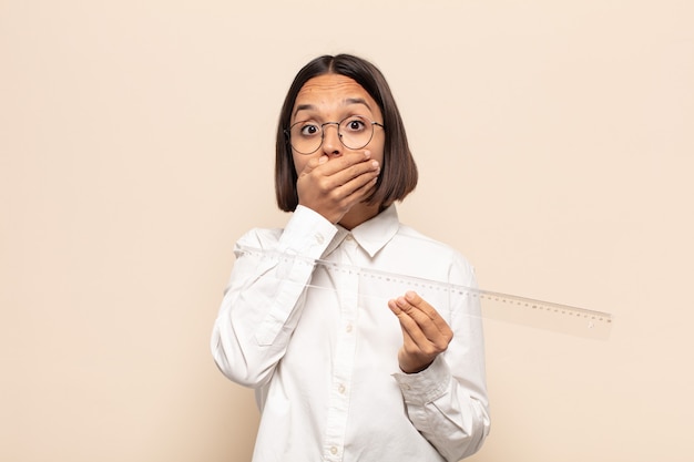 Jonge Latijns-vrouw die mond bedekt met handen met een geschokte, verbaasde uitdrukking, een geheim bewaren of oeps zeggen