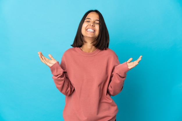 Jonge Latijns-vrouw die op blauwe muur wordt geïsoleerd die veel glimlachen