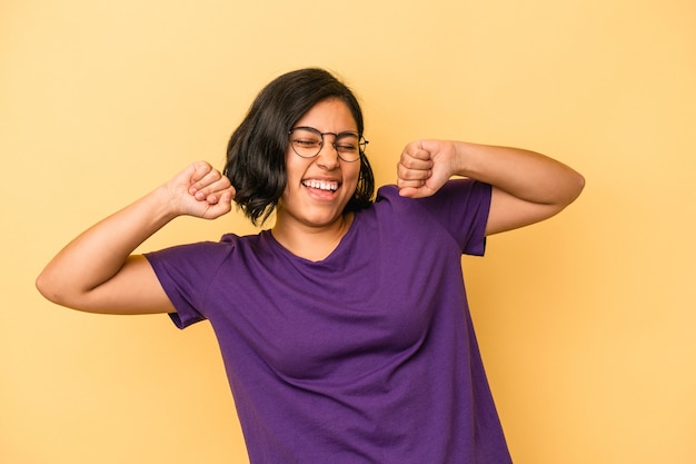 Jonge latijns-vrouw geïsoleerd op gele achtergrond die een speciale dag viert, springt en armen met energie opheft.