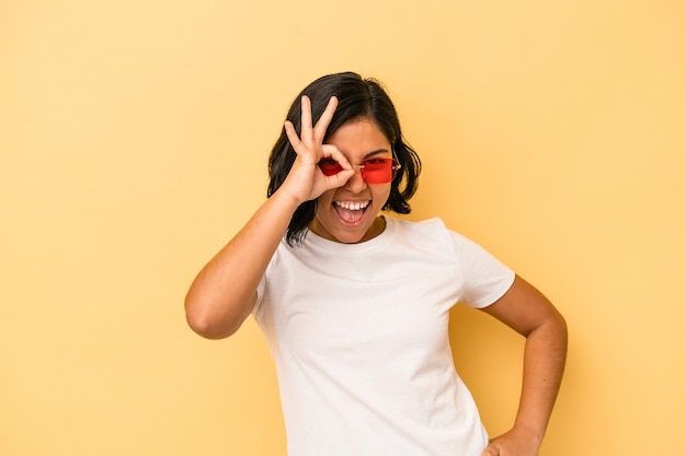 Jonge Latijns-vrouw geïsoleerd op gele achtergrond opgewonden houden ok gebaar op oog.