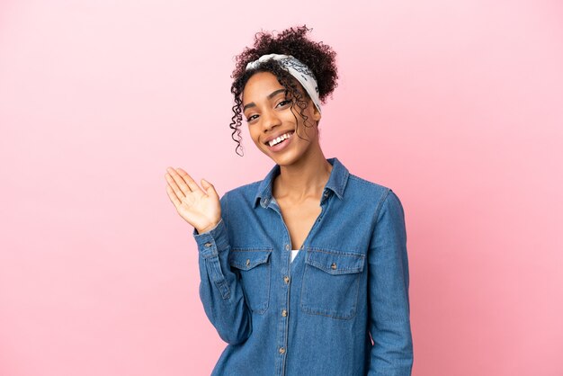 Jonge Latijns-vrouw geïsoleerd op roze achtergrond die met de hand salueert met een gelukkige uitdrukking