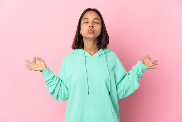 Jonge Latijns-vrouw geïsoleerd op roze muur in zen pose