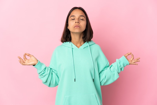 Jonge Latijns-vrouw geïsoleerd op roze muur in zen pose